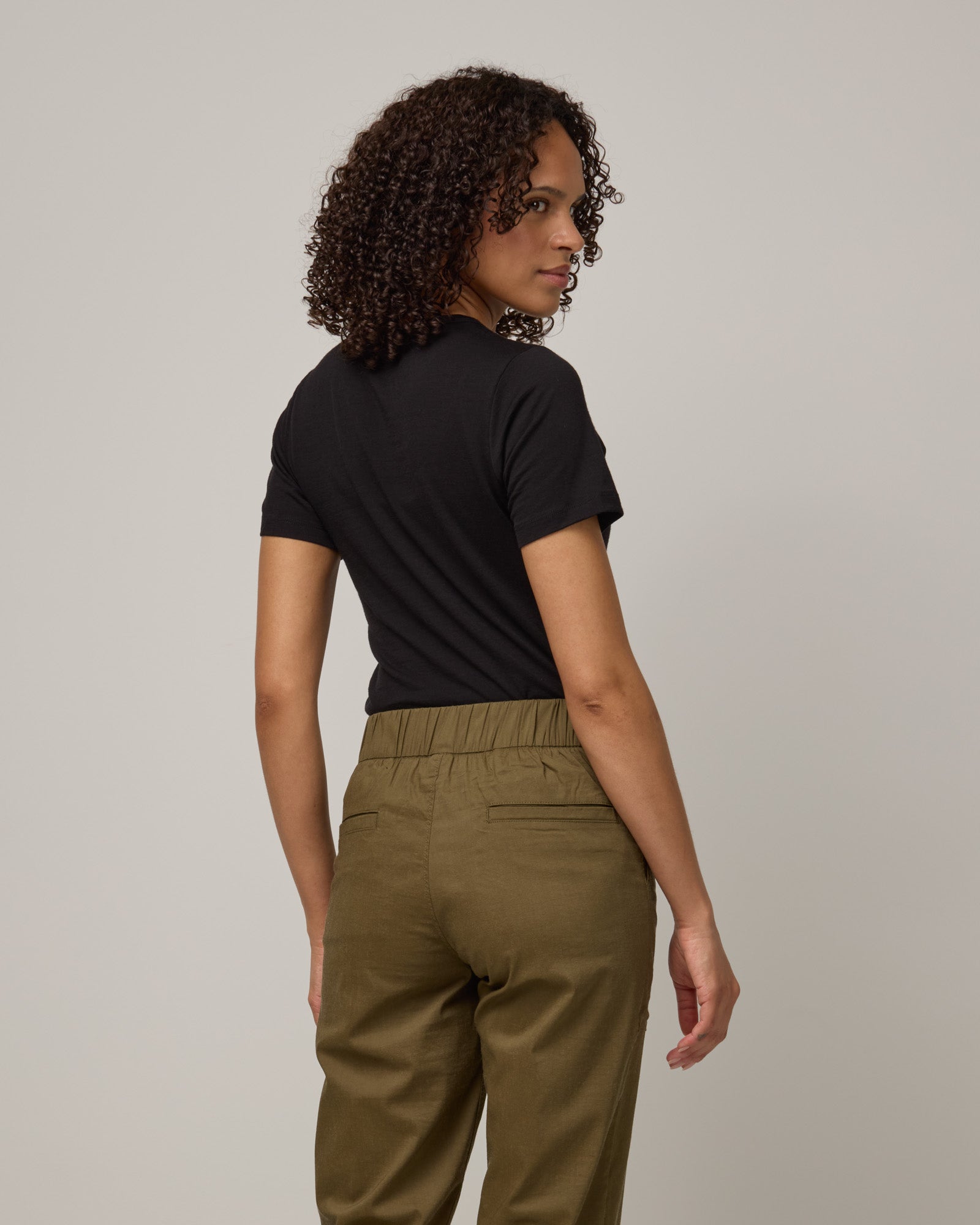 Model wearing Cara 100% Wool Fitted Tee in Black. Cara 100% Wool Fitted Tee is a merino wool short sleeve, crew neck, slim fit tee available in sizes XS-3X.