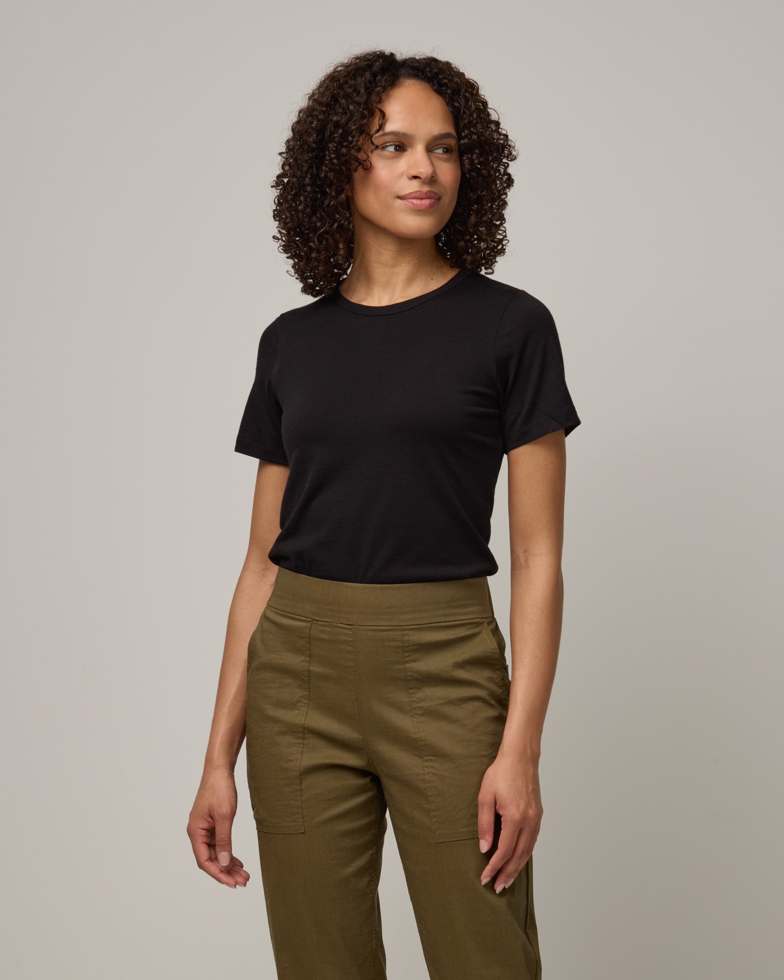 Model wearing Cara 100% Wool Fitted Tee in Black. Cara 100% Wool Fitted Tee is a merino wool short sleeve, crew neck, slim fit tee available in sizes XS-3X.